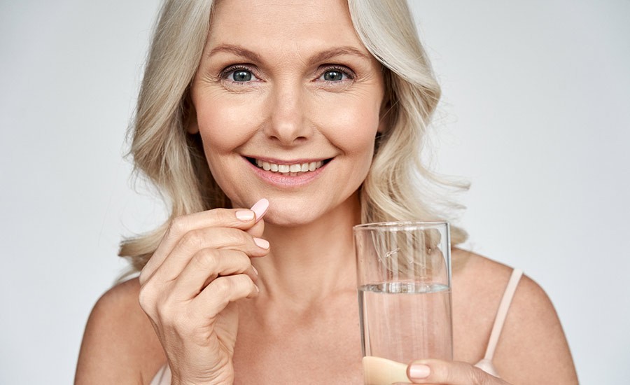 A middle-aged woman takes a supplement and holds a glass of water in her left hand. 